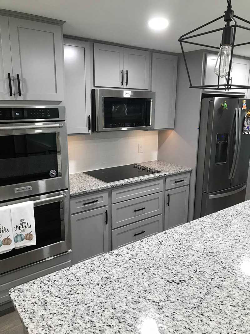 A brand-new kitchen with sparkling stainless steel appliances, grey cabinetry, and gleaming marble countertops, illuminated by modern pendant lights.