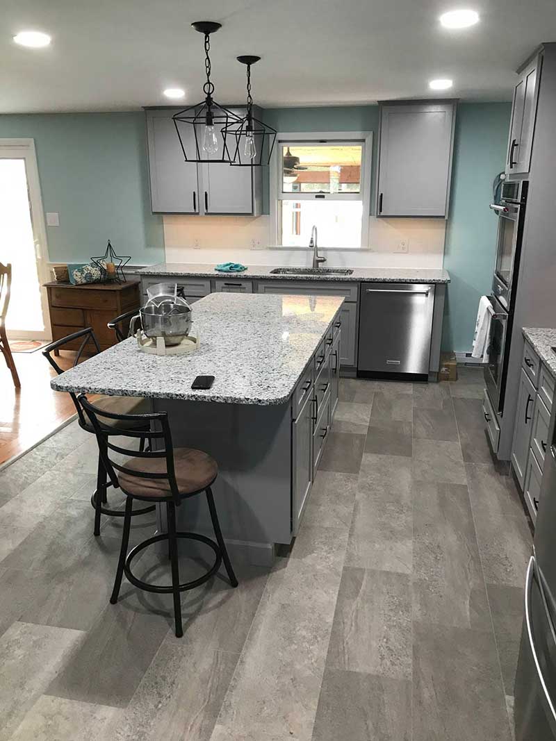 An updated kitchen with lovely vinyl flooring, custom cabinetry, a granite-topped island, and pendant lighting that adds warmth and sophistication.