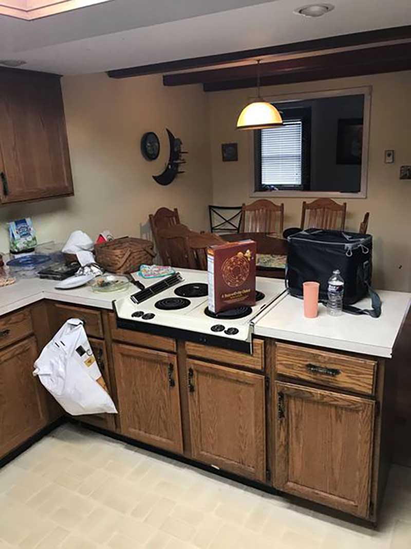 A worn-out kitchen with faded and damaged linoleum flooring, scratched and dented cabinets, and a lack of proper organization.