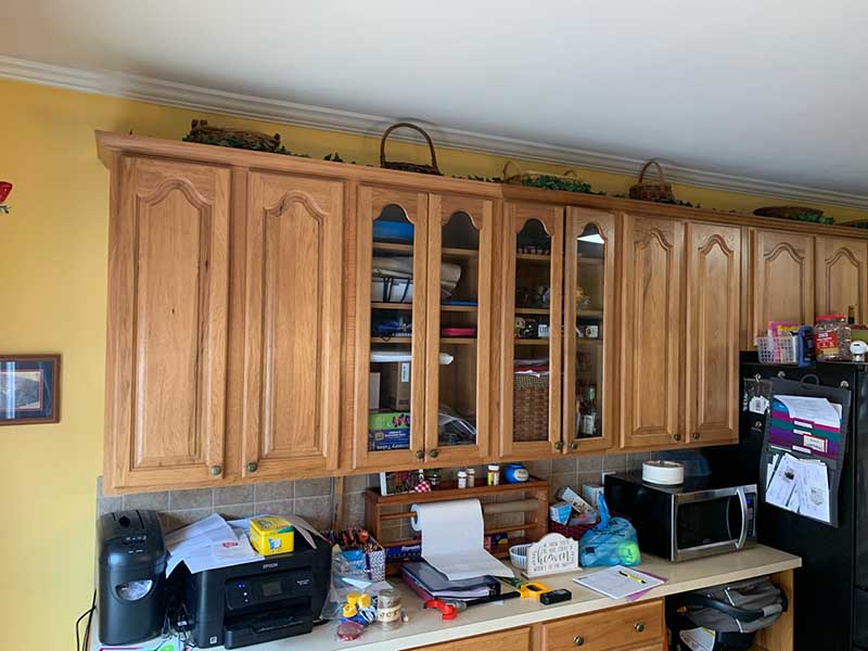 A cramped kitchen with limited counter space, outdated appliances, and cramped, light wooden cabinets.