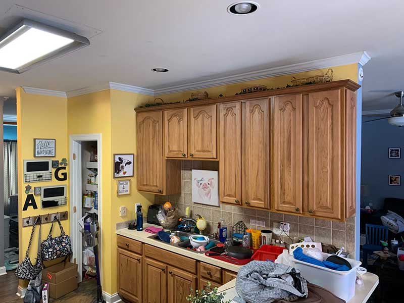 A poorly lit kitchen with dim, yellowed overhead lighting, and a cramped layout featuring outdated appliances.