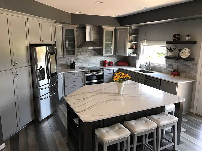 A modern kitchen with new appliances, a stone facade wall, and granite countertops. There is also an island in the center of the kitchen.