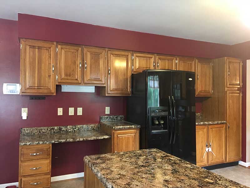An old, outdated kitchen with brown granite countertops and old cabinetry.