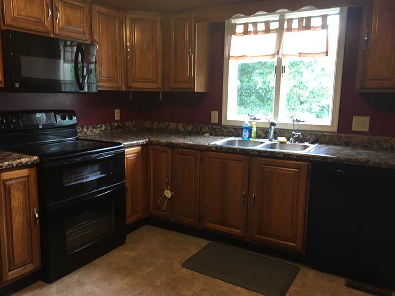 An old kitchen with red walls, worn cabinets, and outdated appliances.
