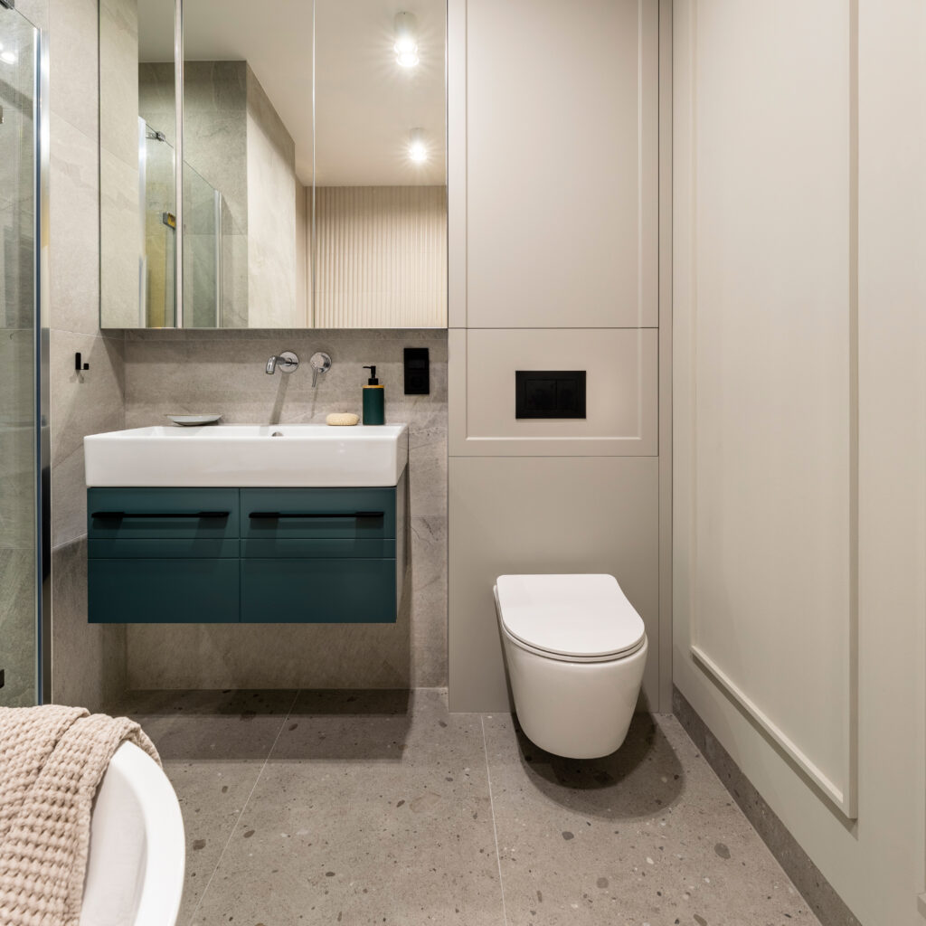 Modern bright bathroom with beige wall. Washbasin with turquoise cupboard and mirror. Wall with molding.